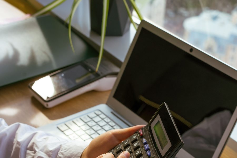 Mains d'une personne utilisant une calculatrice à côté d'un ordinateur portable