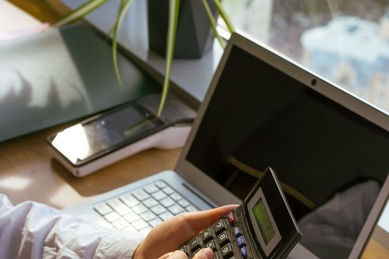 Mains d'une personne utilisant une calculatrice à côté d'un ordinateur portable